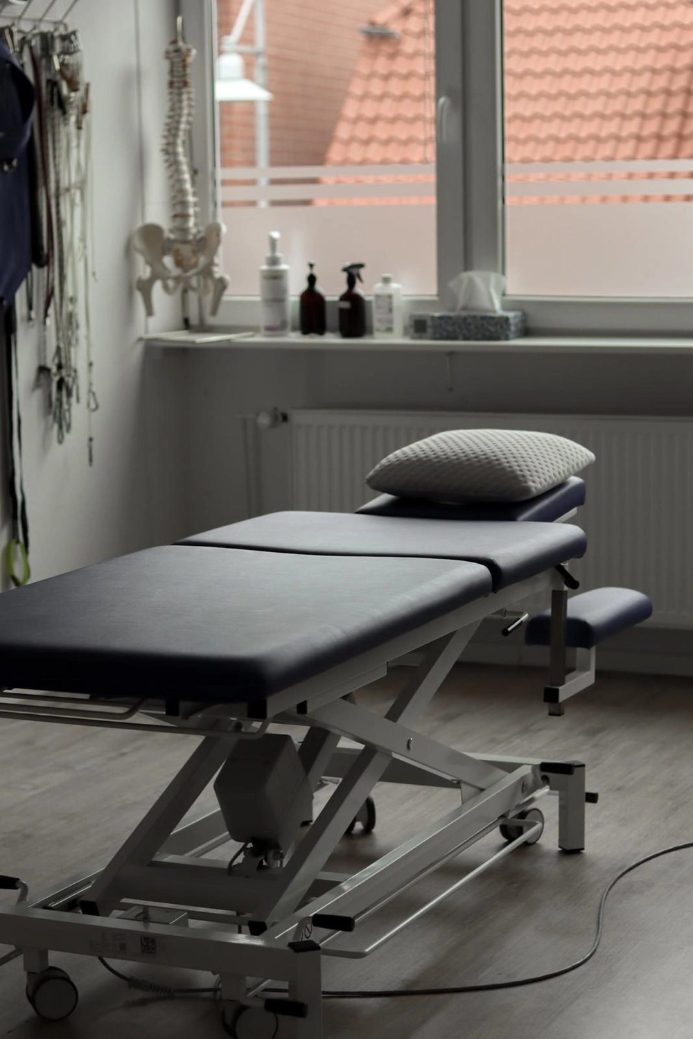 LPZ-Hübner - Physiotherapie und Lymphdrainage - Ein Untersuchungsraum mit verstellbarer Behandlungsliege, medizinisch-anatomischen Modellen von Wirbelsäule und Becken sowie verschiedenen klinischen Verbrauchsmaterialien.