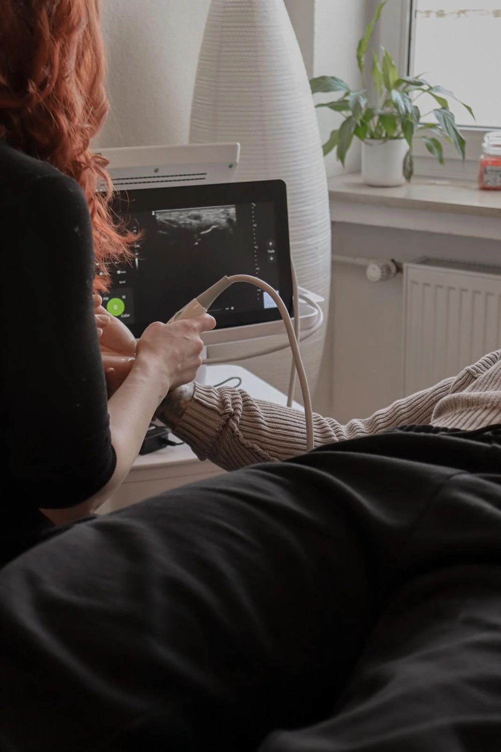 LPZ-Hübner - Physiotherapie und Lymphdrainage - Eine medizinische Fachkraft mit roten Haaren führt eine Ultraschalluntersuchung an einem Patienten durch, der in einem hell erleuchteten Raum liegt.